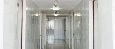 Um corredor comprido e estreito, com paredes brancas e chão reluzente, que leva a uma porta no final.