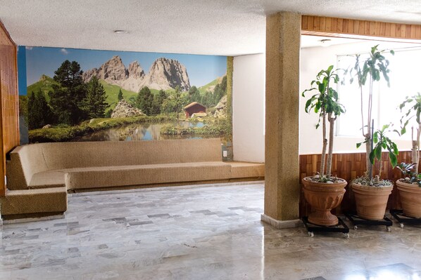 A lobby with a mural of a mountain landscape, a beige sofa, and terracotta planters with plants. - Hotel Central Irapuato (Irapuato)