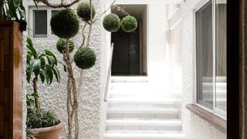 A white building with a staircase leading to a door, surrounded by potted plants and spherical topiary.