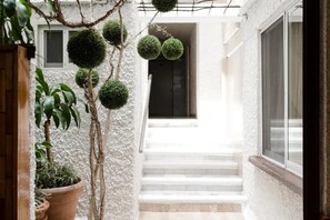 A white building with a staircase leading to a door, surrounded by potted plants and spherical topiary. - Hotel Central Irapuato (Irapuato)