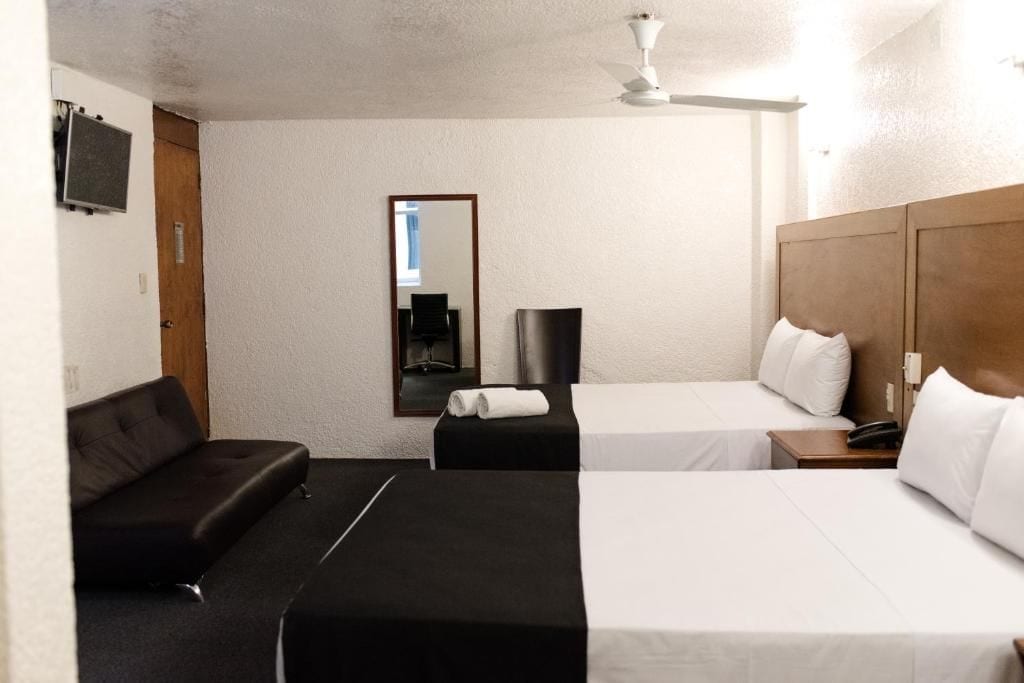 Habitación de hotel con sofá, dos camas, espejo, ventilador de techo y televisor de pantalla plana.