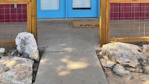 Een blauwe deur met een deurmat, houten pilaren en een metalen poort.
