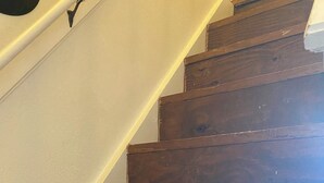 Una escalera de madera con una pared blanca a un lado y un suelo de madera oscura al otro.