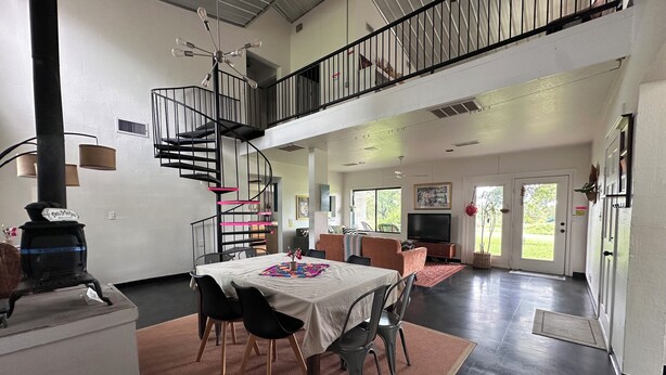A spacious living area with a dining table, chairs, a spiral staircase, and a large window.