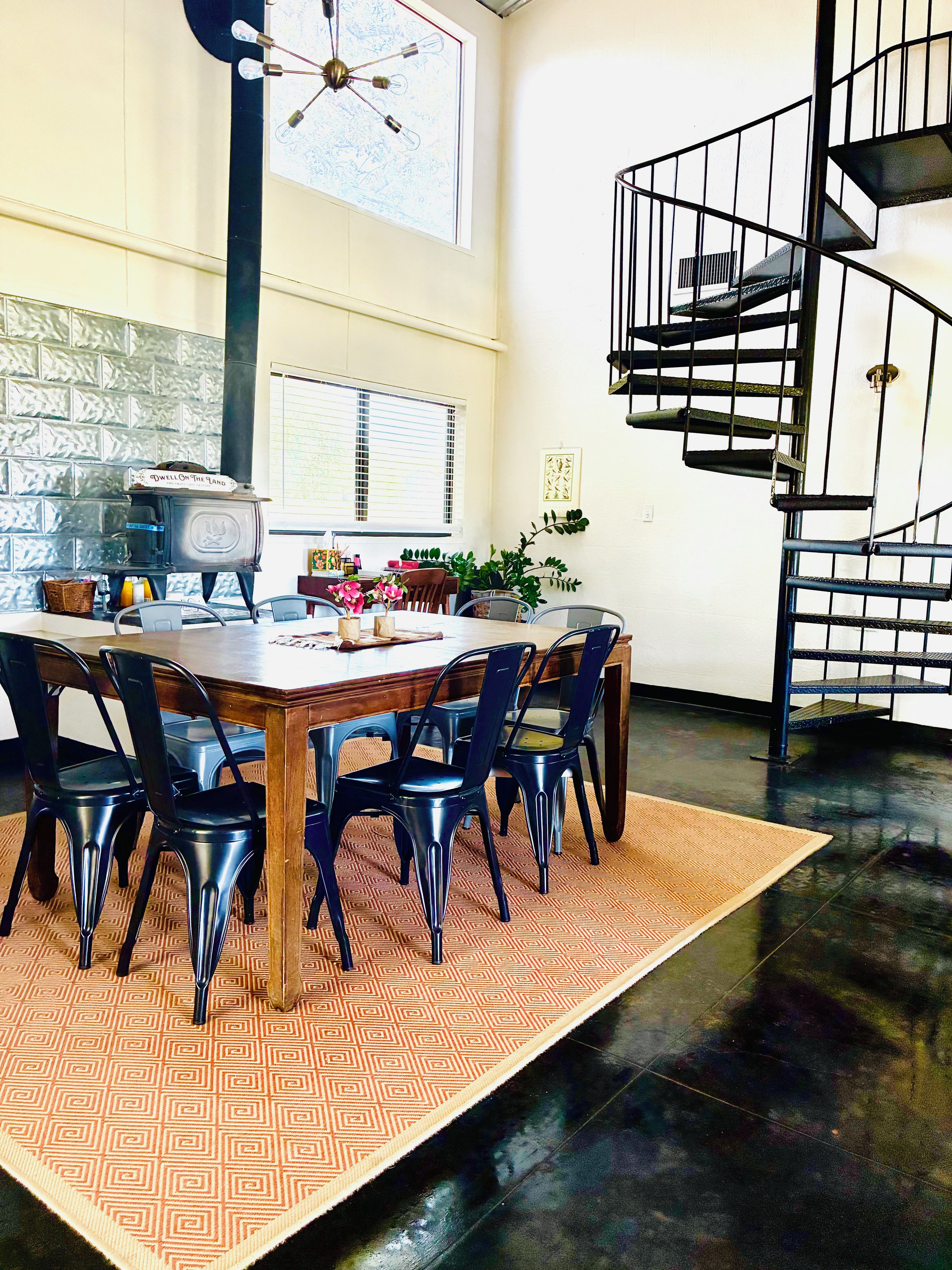 A dining area with a wooden table, black chairs, a patterned rug, a stove, and a spiral staircase.