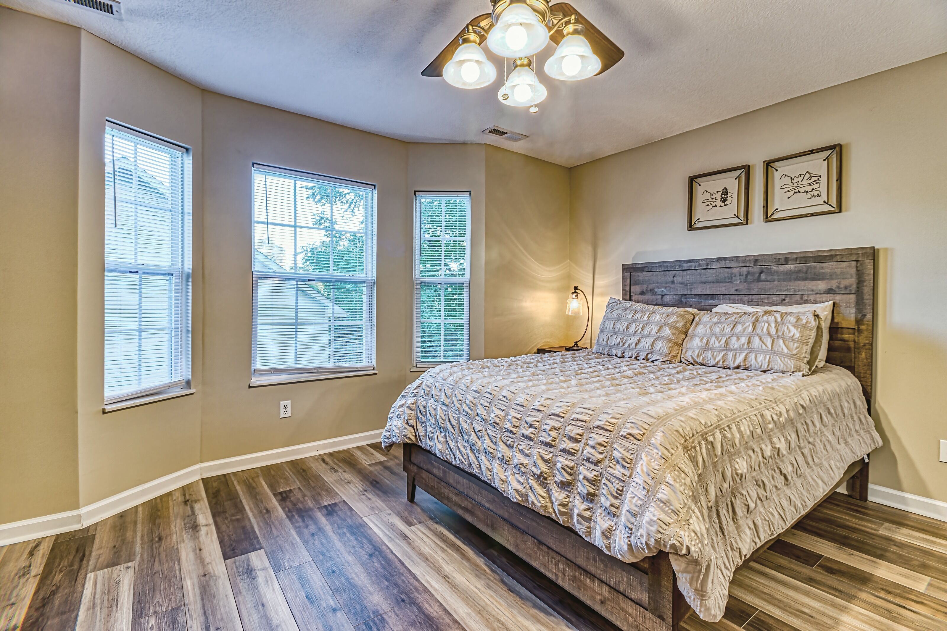 A bedroom with a wooden bed, three windows, a ceiling fan, and two wall-mounted lights.