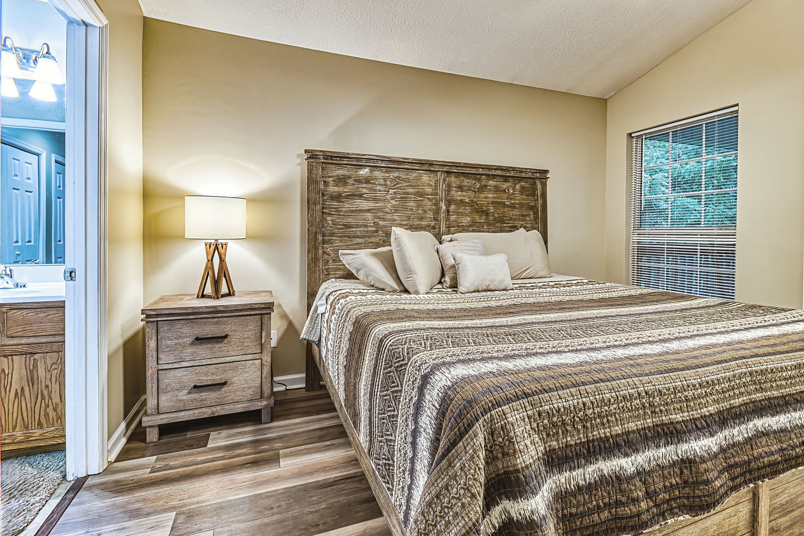 A bedroom with a wooden headboard, a bedside table with a lamp, and a window with blinds.