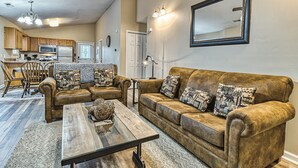 A living room with a brown sofa set, a coffee table, and a kitchen in the background. - Smoky Mountain Chalet | Pool | Steps to Parkway (Pigeon Forge)