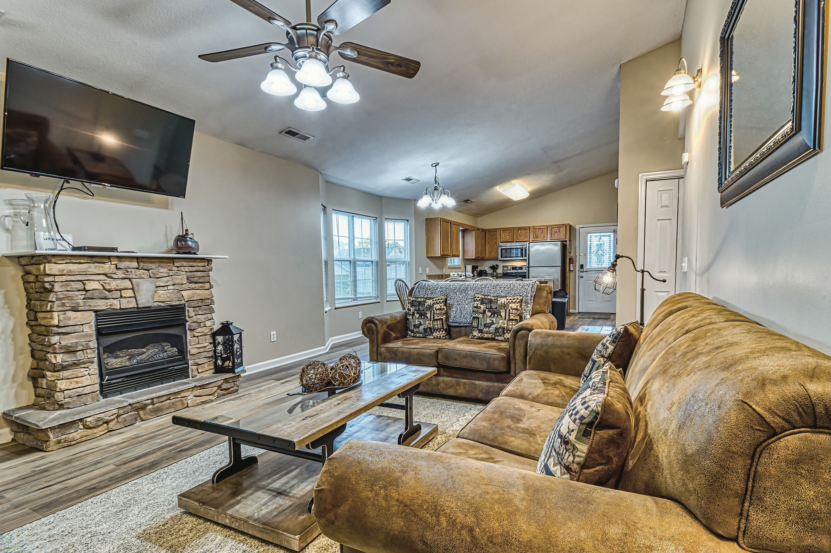 A living room with a stone fireplace, a ceiling fan, and a flat-screen TV.