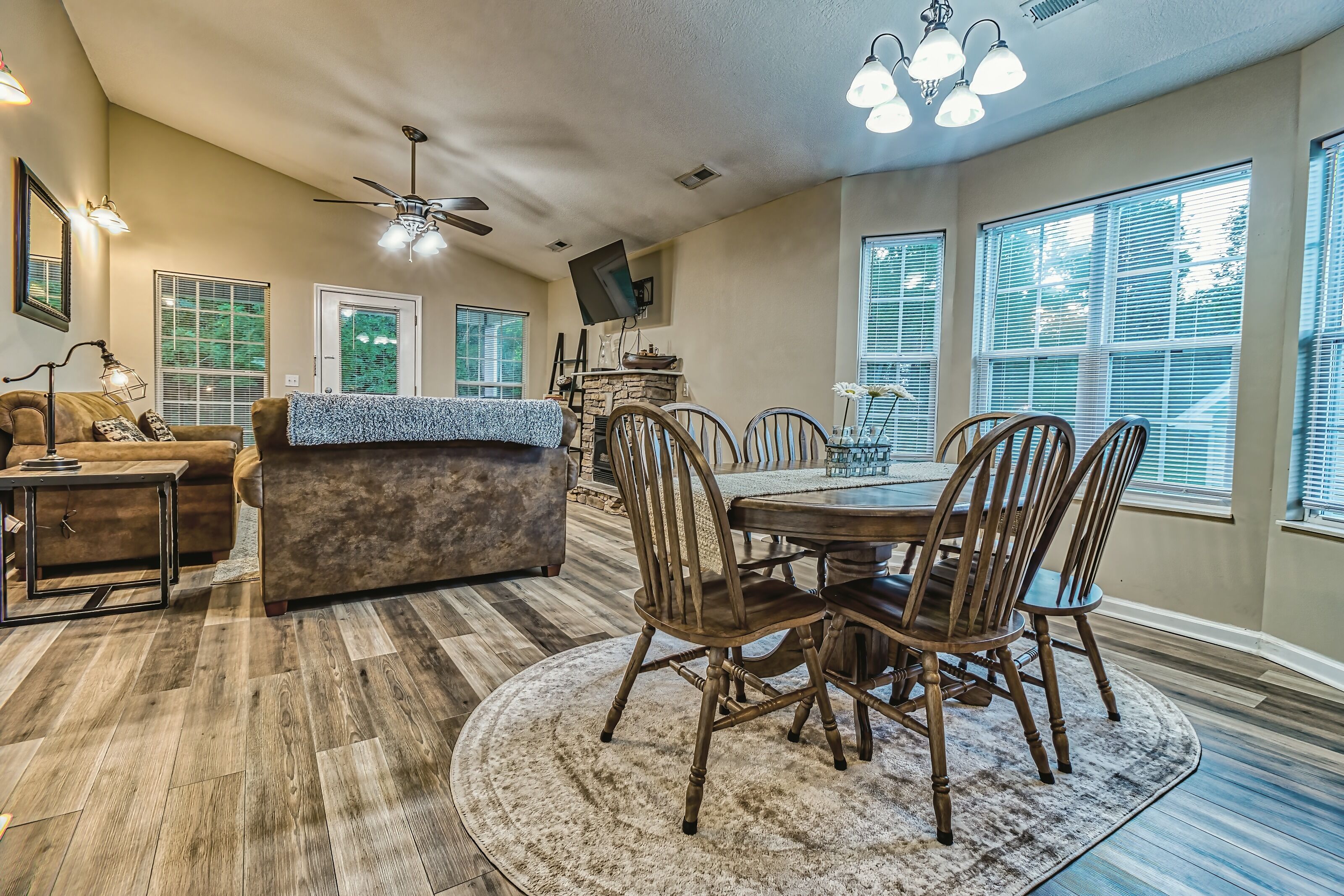 A spacious dining area with a round table and wooden chairs, a sofa, and a ceiling fan.