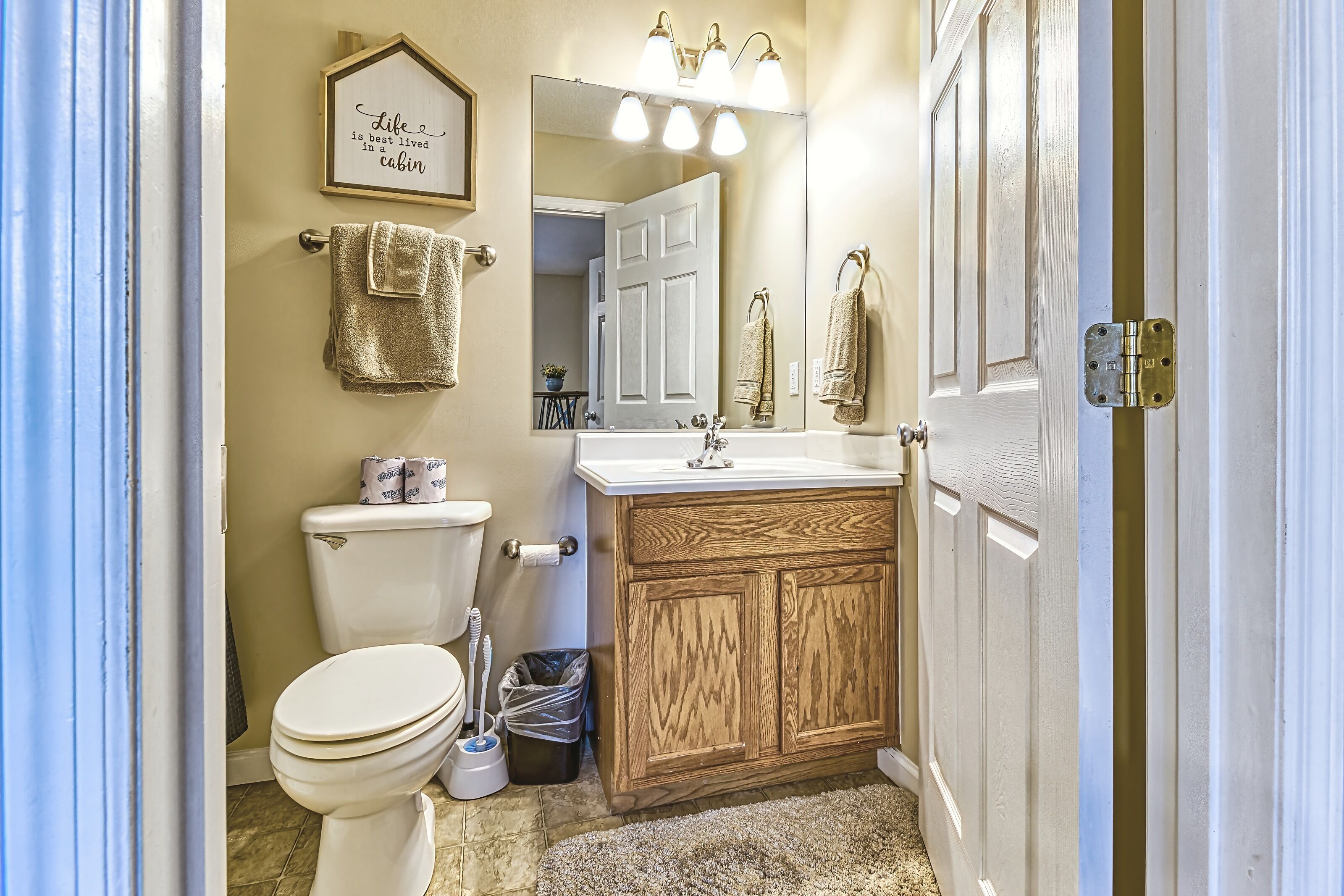 A bathroom with a toilet, sink, mirror, and wooden cabinets.