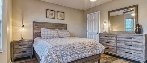 Een slaapkamer met een houten bed, een nachtkastje, een dressoir, een plafondventilator en een grote spiegel.