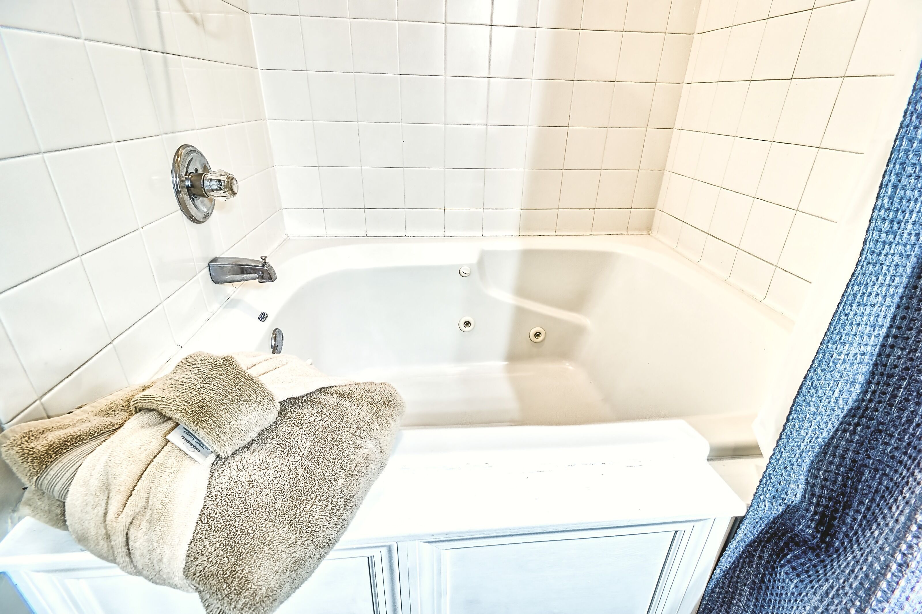 Ein Badezimmer mit weißen Fliesen, einer Badewanne, einer Duschvorhang und einem Handtuchhalter mit einem Handtuch.