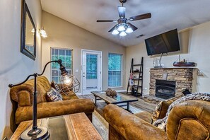 A living room with a stone fireplace, leather sofas, a coffee table, and a television mounted on the wall.