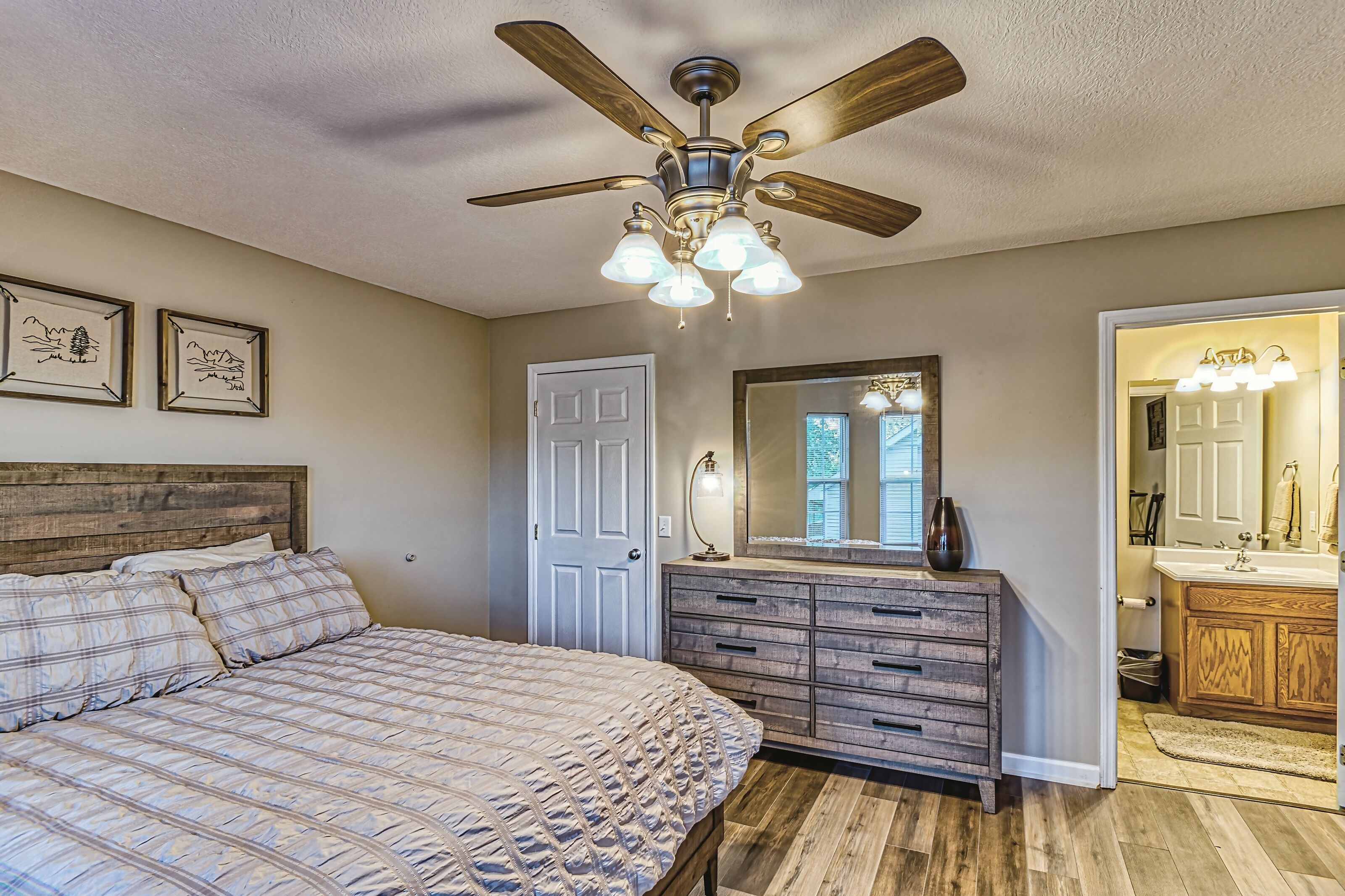 A bedroom with a bed, a dresser, a ceiling fan, and a bathroom visible through an open door.