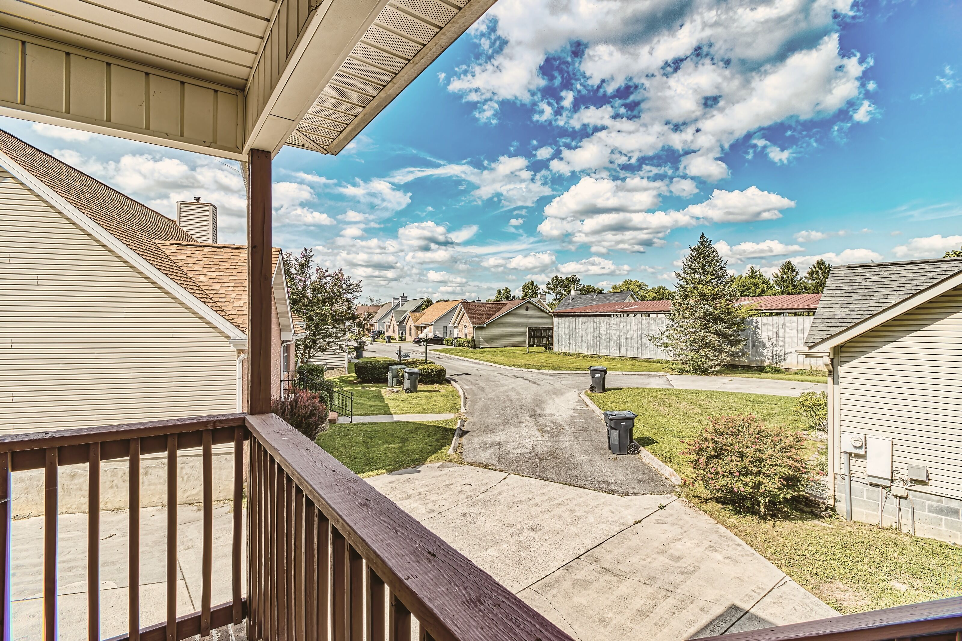 A residential street with houses, a clear sky, and a wooden deck.