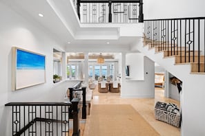 A spacious interior with a high ceiling, a staircase with black railings, and a view to the outside.
