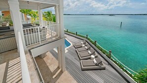 A deck with lounge chairs overlooking a clear blue sea, a covered seating area with cushions, and a wooden deck. - Oceanfront, Private Dock, Paddle Boards, Feb Pt Access!! (Georgetown, BS)