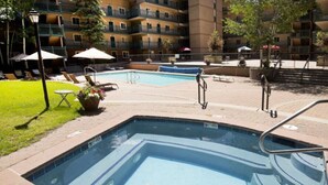 A rectangular swimming pool with a tiled edge, surrounded by a brick deck. There are lounge chairs and umbrellas in the background, and a multi-story building with balconies. - Vail/Lionshead 2-bedroom with Pool  & Hot Tub (Vail)