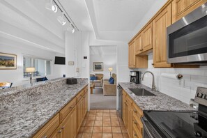 Une cuisine dotée de plans de travail en granit, d’armoires en bois, d’un four à micro-ondes en acier inoxydable et d’une cuisinière noire.