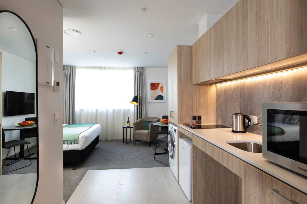 Une chambre d’hôtel moderne équipée d’une kitchenette, d’un lit, d’un bureau et d’une télévision.