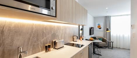 Une cuisine moderne équipée d’un four à micro-ondes, d’un grille-pain et d’un évier intégrés. Un coin repas avec une table et des chaises est également disponible.