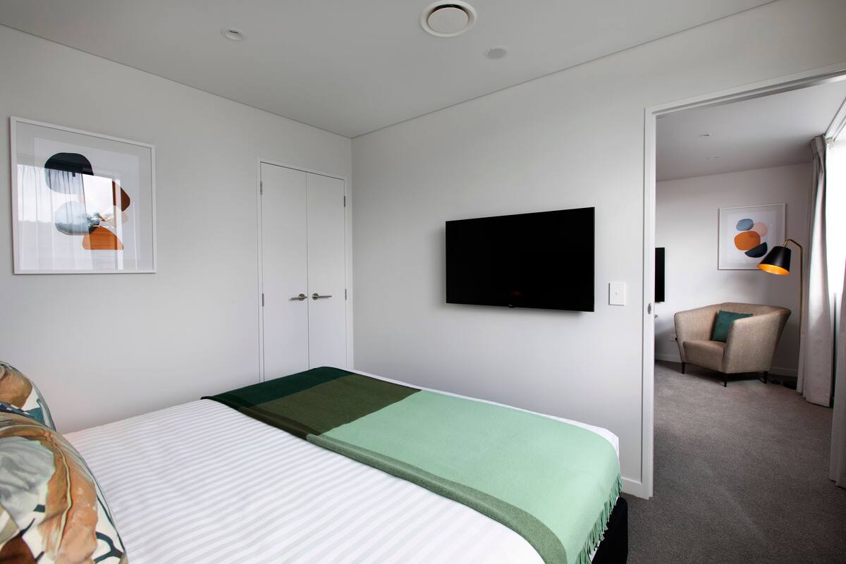 Une chambre d’hôtel équipée d’un lit, d’un téléviseur à écran plat, d’une chaise et d’œuvres d’art accrochées aux murs.