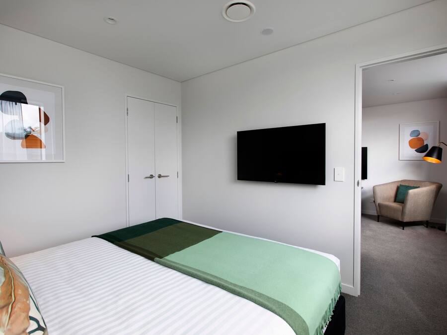 A hotel room with a bed, a flat-screen TV, a chair, and artwork on the walls.