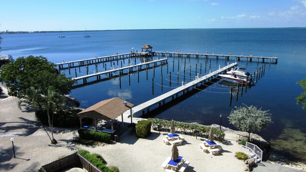 A pier extending into calm waters with boats docked, surrounded by a sandy beach with lounge chairs and a small pavilion. - Top floor condo in Key Largo with spectacular Sunset views (Key Largo)