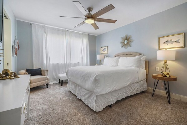 A bedroom with a large bed, a ceiling fan, a desk, and a chair.