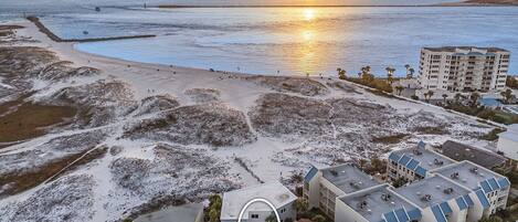 Vista aérea de una zona costera con playa, aparcamiento y un complejo de edificios con varios pisos y balcones.