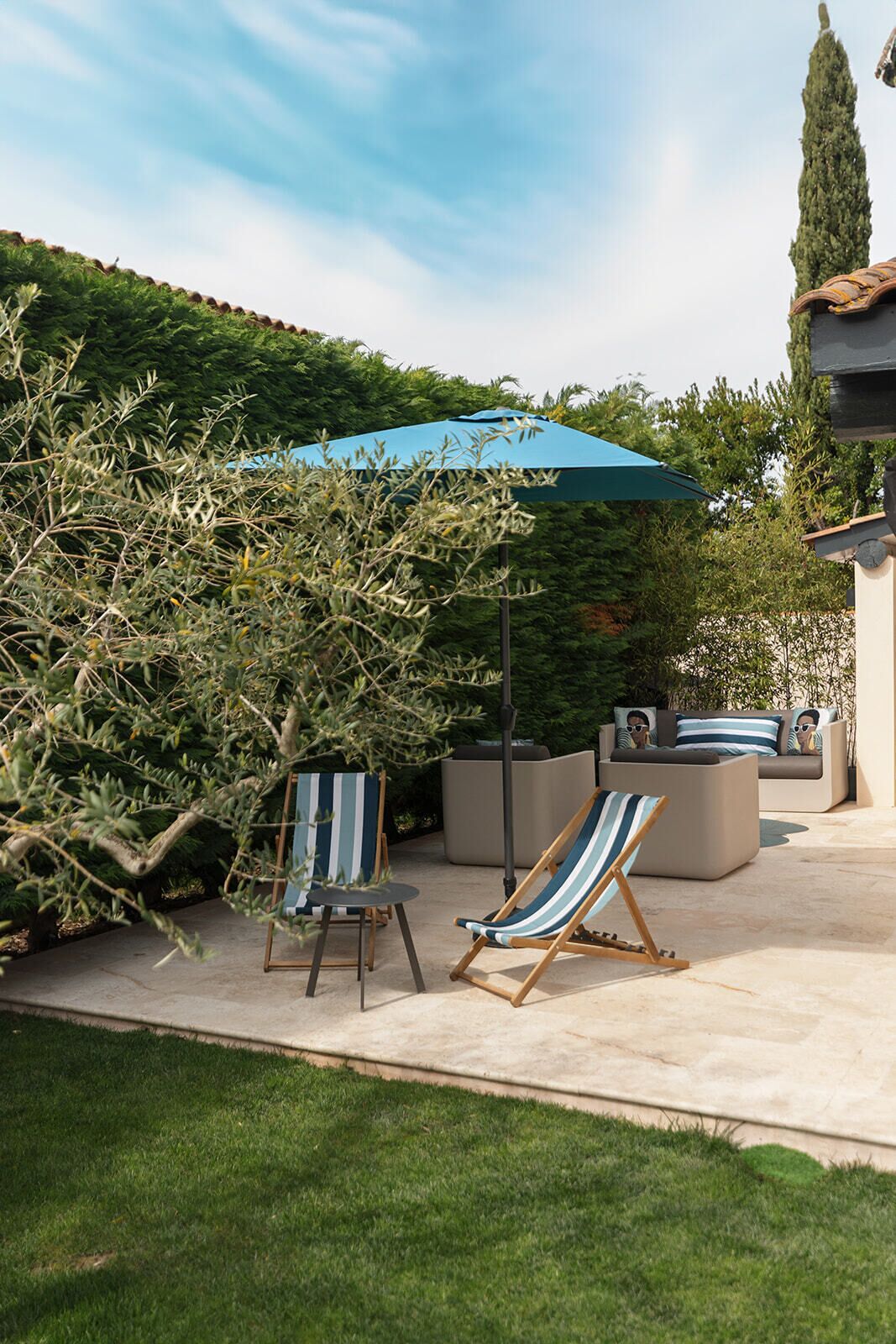 Une terrasse extérieure avec deux chaises longues à rayures, un parasol bleu et un canapé moderne.