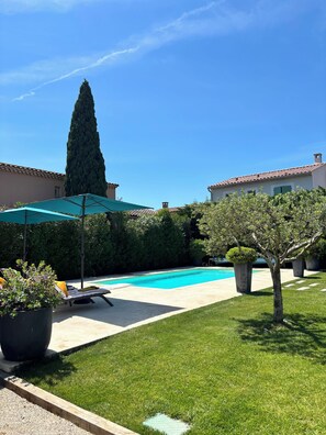 Une piscine entourée de chaises longues et de parasols, avec une pelouse et des arbres bien entretenus.
