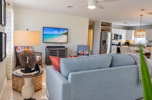 A modern living room with a sofa, a television, and a kitchen in the background.