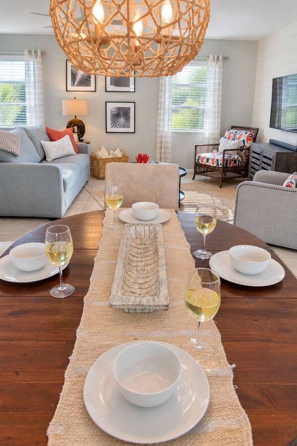 A dining area with a long wooden table set for four, featuring a central decorative piece, white plates, and glasses of white wine.