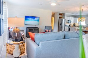 A modern living room with a grey sofa, a television, and a kitchen area in the background.