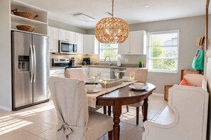 Une cuisine moderne avec des meubles blancs, des appareils en acier inoxydable et un coin repas comprenant une table et des chaises en bois.