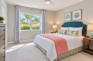 A bedroom with a bed, nightstands, a window with curtains, a ceiling fan, and framed artwork on the wall.