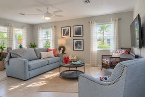 A living room with a sofa, armchair, coffee table, and a flat-screen TV mounted on the wall.