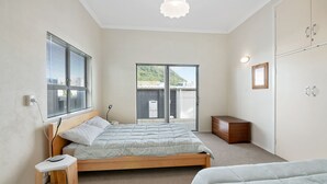 Ein Schlafzimmer mit zwei Betten, einem Nachttisch, einem Kleiderschrank und Blick ins Freie durch eine Schiebetür.