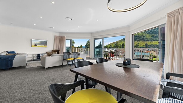 Ein modernes Hotelzimmer mit großem Esstisch, bequemen Sitzgelegenheiten, einer Couch und Blick auf eine Berglandschaft.