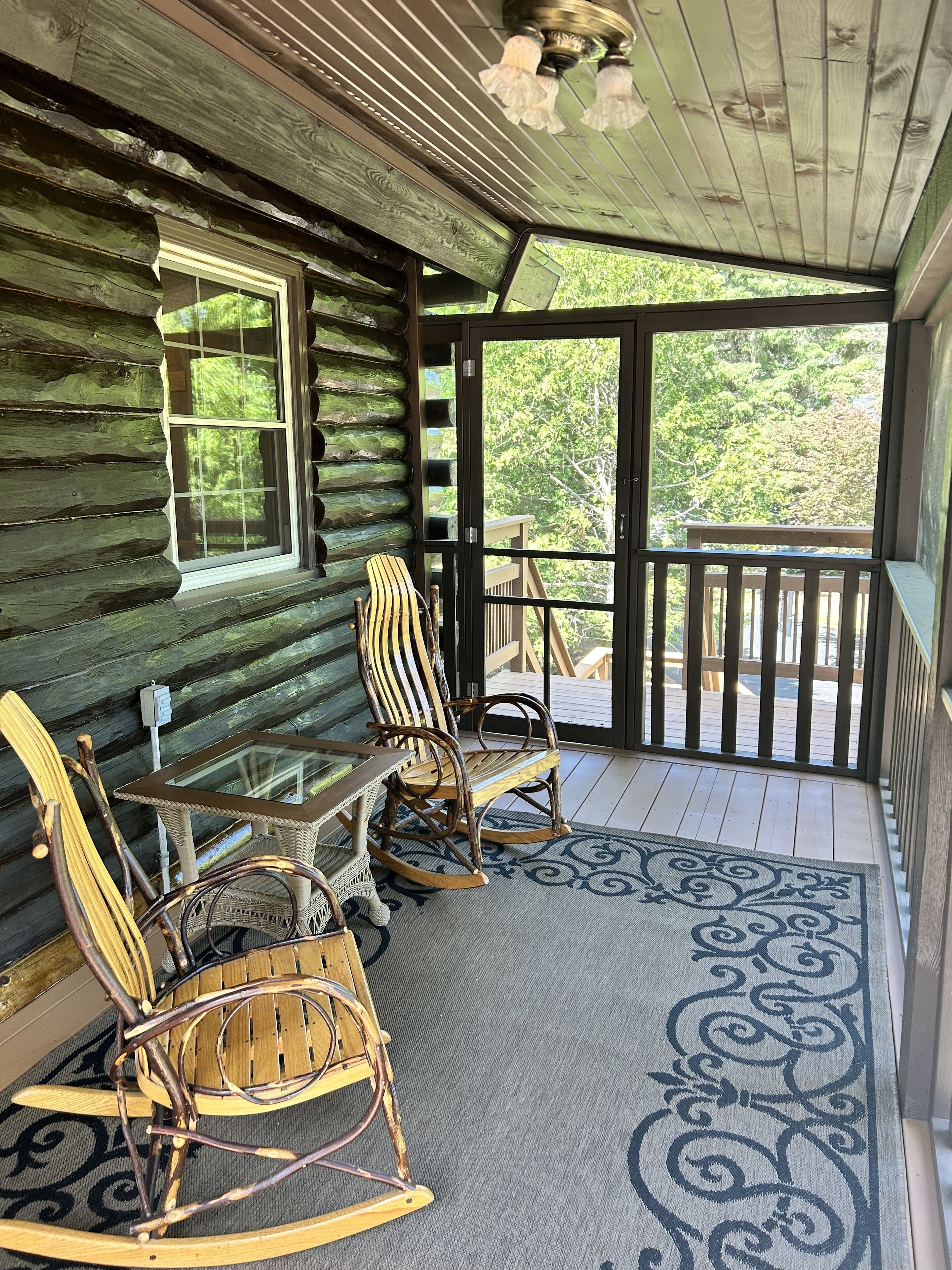 Une cabane en rondins dotée d’un porche avec des fauteuils à bascule et une table en verre.