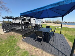 A deck with outdoor seating and a covered area, adjacent to a recreational vehicle. - Waterfront at Sherkston Shores Resort (Port Colborne)