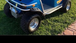 A blue golf cart with a metal frame and a seat, parked on grass.