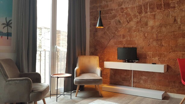 Ein modernes Wohnzimmer mit Backsteinwand, einem an der Wand befestigten Fernseher, einem grauen Sessel, einem kleinen Beistelltisch und roten Sesseln.