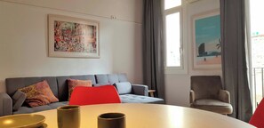 Un salon avec un canapé gris, un fauteuil rouge et une table ronde sur laquelle sont posées deux tasses.