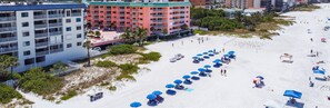 Una playa con hileras de sombrillas azules y sillas, un edificio de varios pisos con balcones, y una zona de arena.