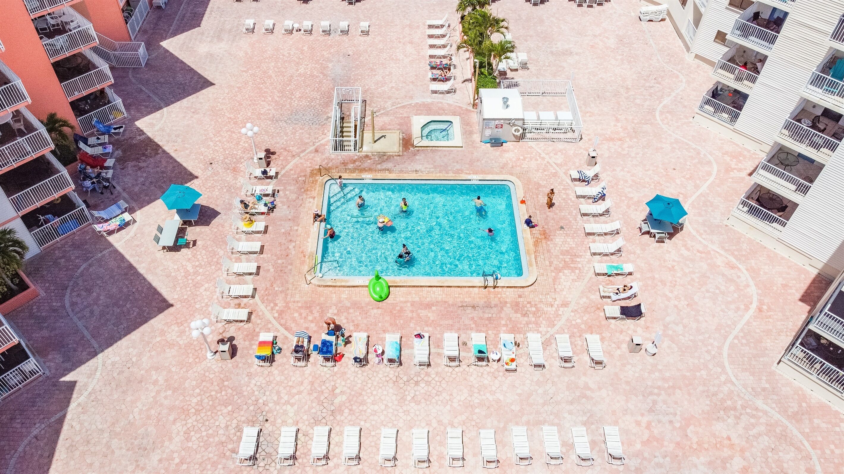 An aerial view of a hotel with a central swimming pool surrounded by sun loungers and a small hot tub.