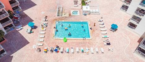 An aerial view of a hotel with a central swimming pool surrounded by sun loungers and a small hot tub.