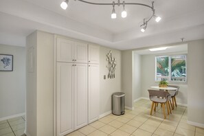 A modern kitchen with white cabinets, a stainless steel trash can, and a dining area with a table and chairs.